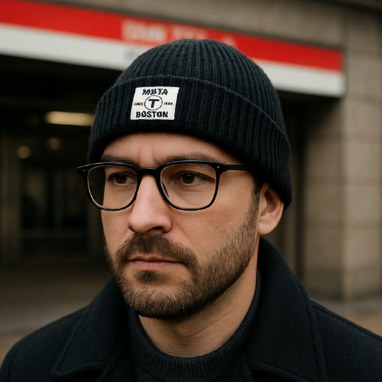 Man wearing a black beanie hat with a rectangular woven patch with the Boston MBTA logo