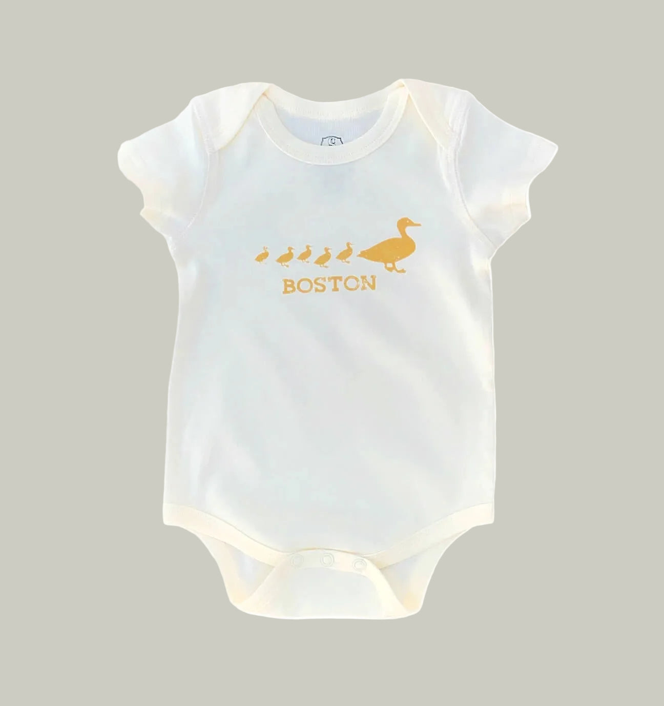 A natural ivory colored short-sleeve baby bodysuit featuring a golden-brown graphic of a duck family and the word 'BOSTON' printed on the chest, displayed against a solid tan background.