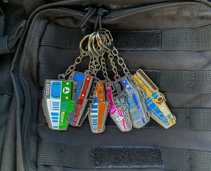 Six Boston MBTA vehicle metal keychains clipped to backpack
