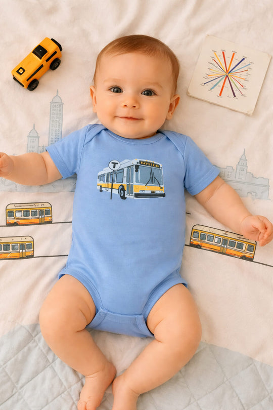 happy baby boy wearing carolina blue Boston MBTA onesie lying on his back